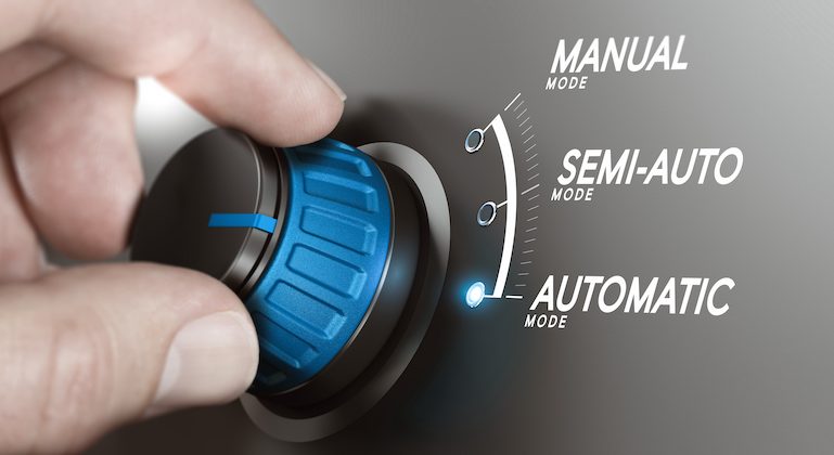 Hand turning a knob over grey background and selecting the automatic mode.