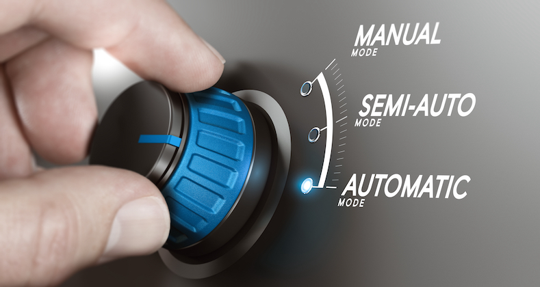 Hand turning a knob over grey background and selecting the automatic mode.