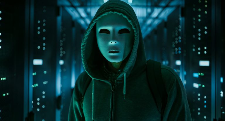 Masked Hacker in a Hoodie Standing in Corporate Data Center