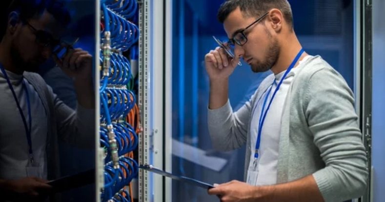 young man standing by server cabinet while working with supercomputer in data center